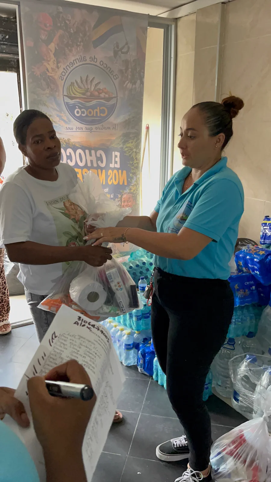 Voluntaria del Banco de Alimentos del Chocó entregando un mercado en mano frente al pendón de la campaña