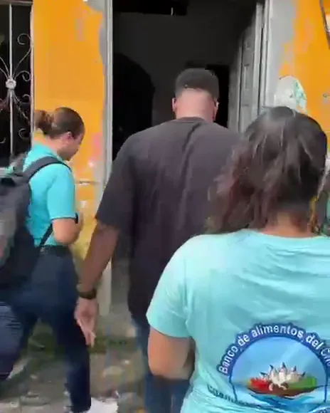 El equipo del Banco de Alimentos del Chocó entra de espaldas por la puerta de una casa amarilla con la pintura desconchada
