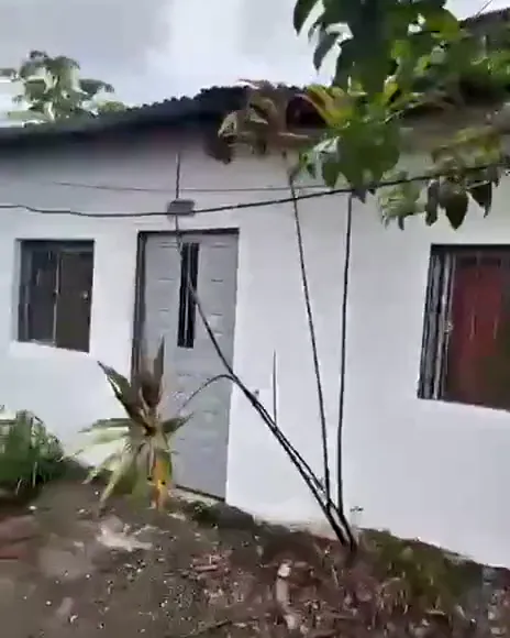 Una casa de paredes blancas, con puerta metálica gris y ventanas con reja